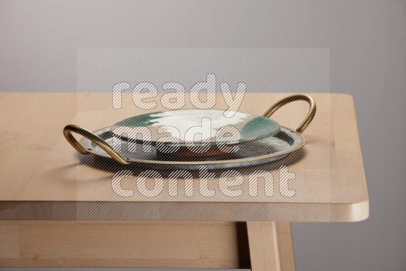multicolored plate placed on a rounded stainless steel tray with golden handels on the edge of wooden table