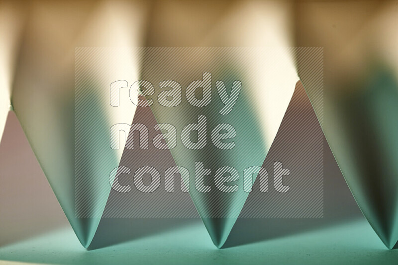 A close-up abstract image showing sharp geometric paper folds in green gradients and warm tones