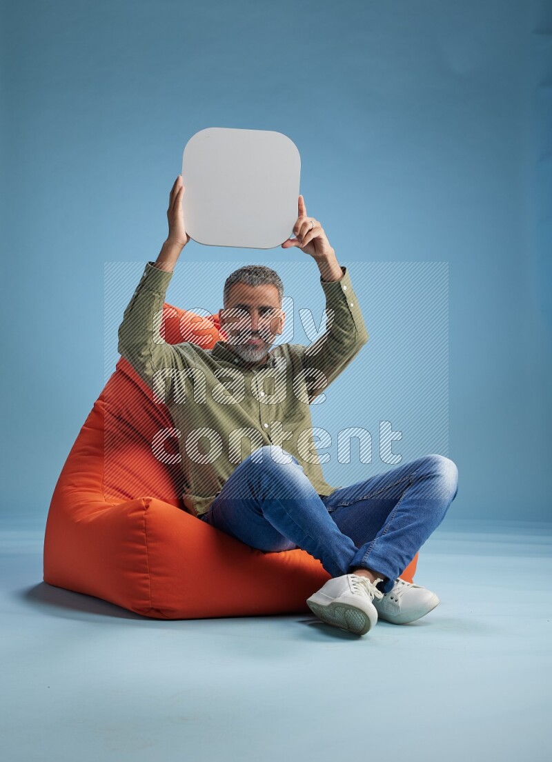 A man sitting on a orange beanbag and holding social media sign
