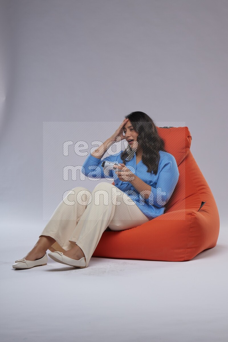 A woman sitting on an orange beanbag and gaming with joystick