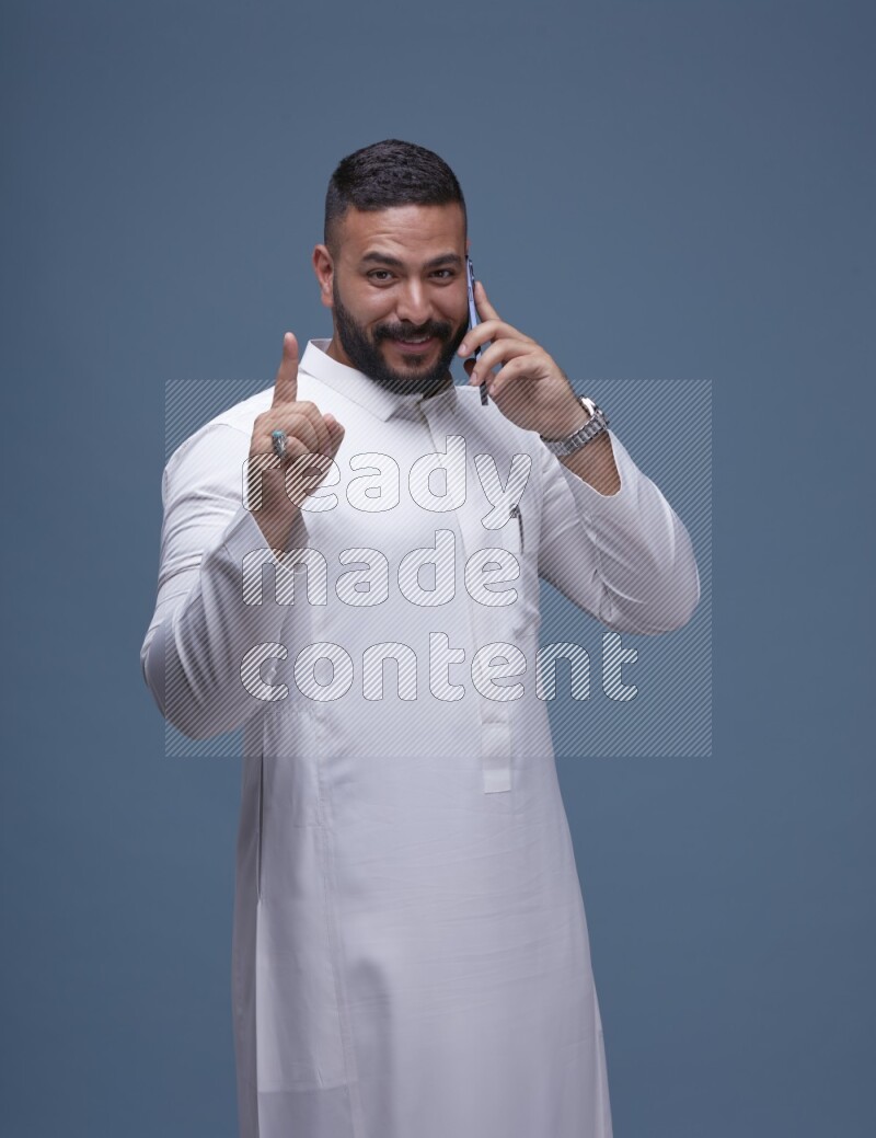 A Saudi man calling on blue background wearing Saudi Thob
