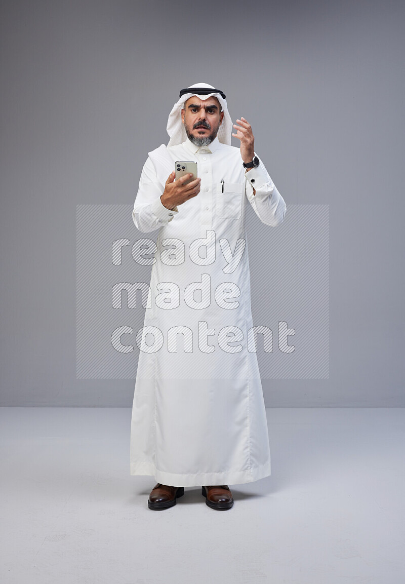 رجل سعودي يرتدي ثوب وشماغ ابيض يحمل هاتف جوال