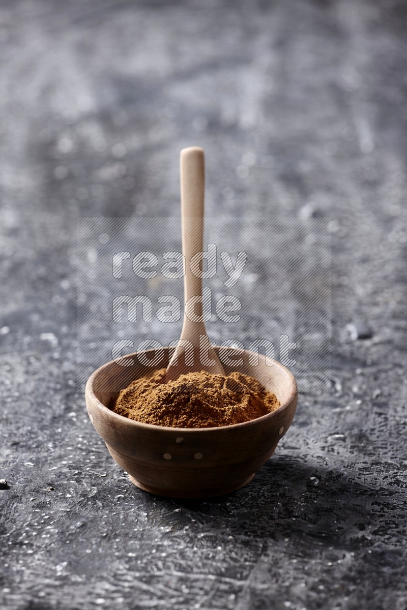 Wooden bowl full of cinnamon powder with a wooden spoon on a textured black background in different angles