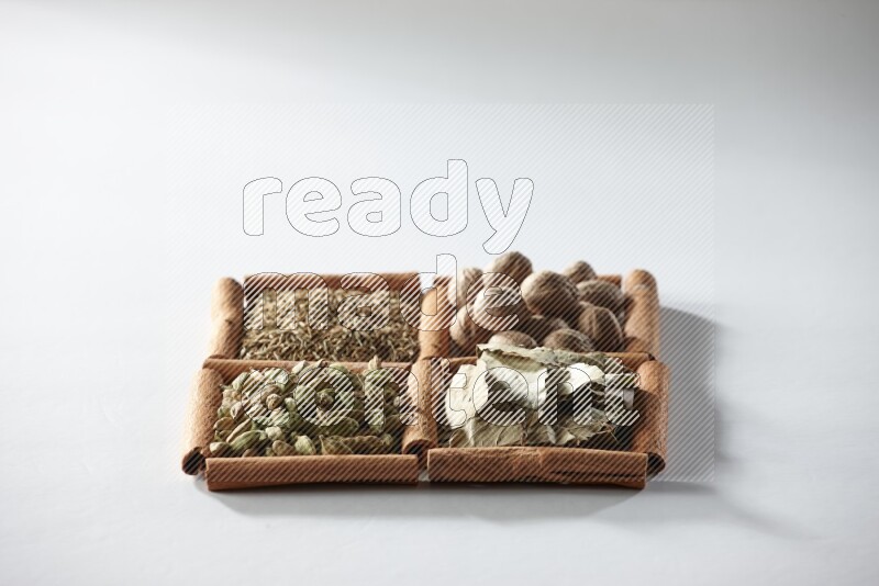 4 مربعات من أعواد القرفة ممتلئة بجوزة الطيب وأوراق الغار وحبوب الهيل والكمون على أرضية بيضاء