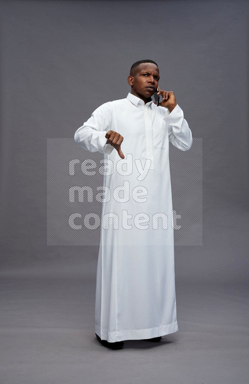 Saudi man wearing thob standing talking on phone on gray background