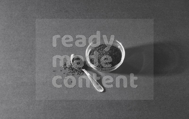 وعاء زجاجي ممتلئ ببذور حبة البركة مع ملعقة معدنية مليئة بحبة البركة علي خلفية سوداء