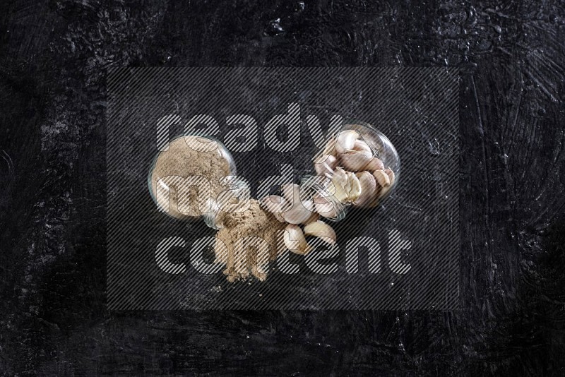 2 glass spice jars full of garlic cloves and powder flipped and the garlic came out on a textured black flooring in different angles