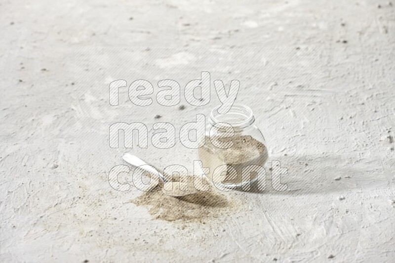 Herbal Glass jar full of white pepper powder and metal spoon full of powder on textured white flooring