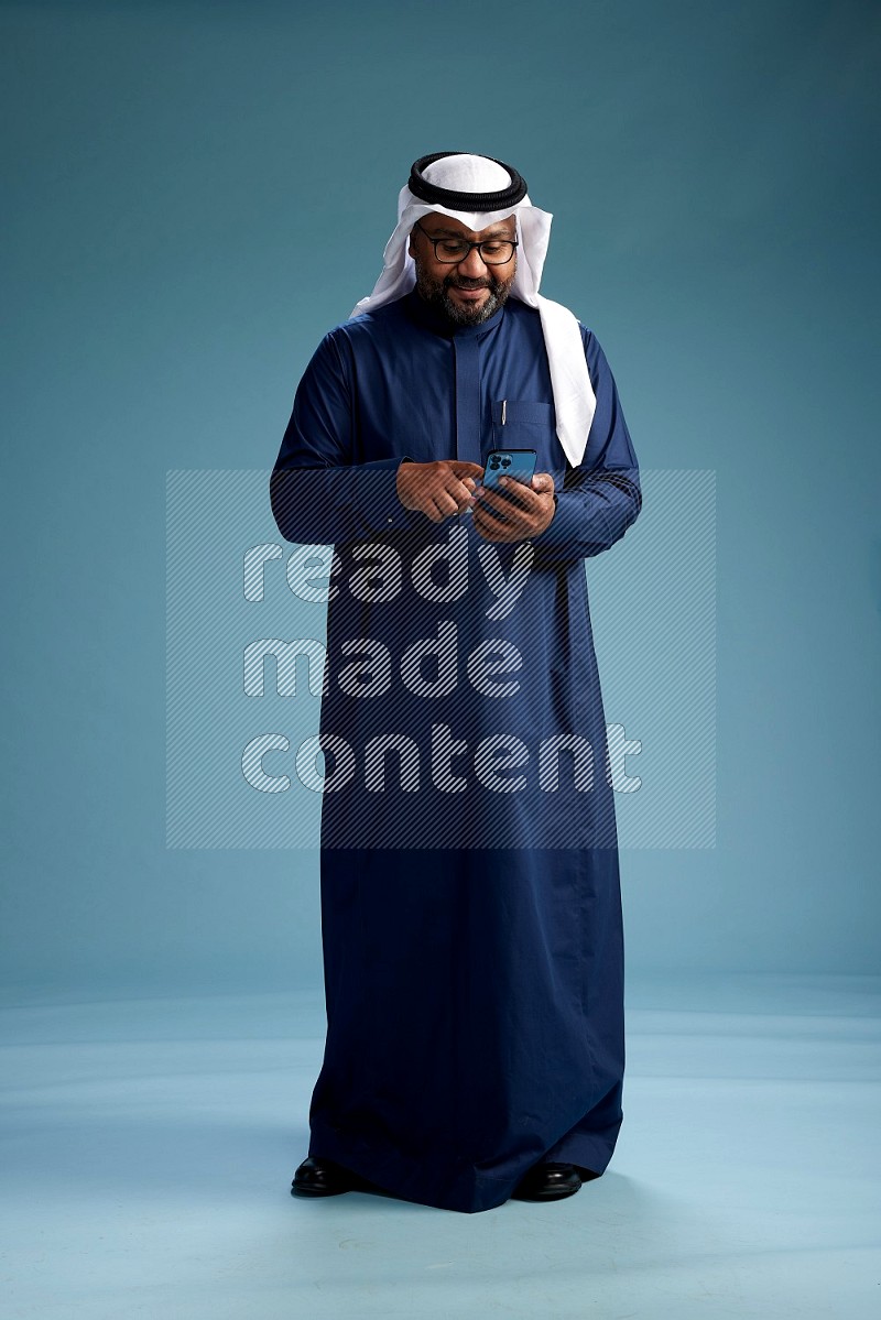 Saudi Man with shimag Standing holding ATM card while talking on phone on blue background