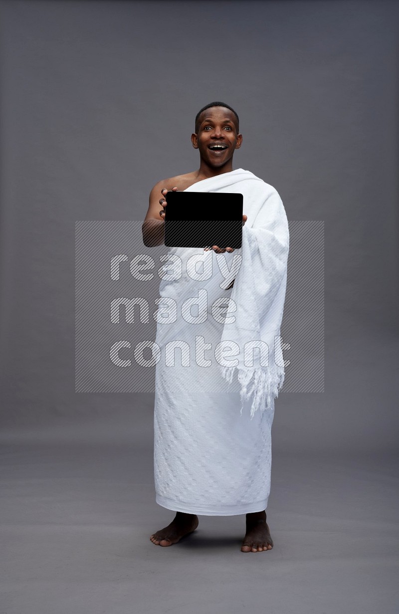 A man wearing Ehram Standing showing tablet to camera on gray background