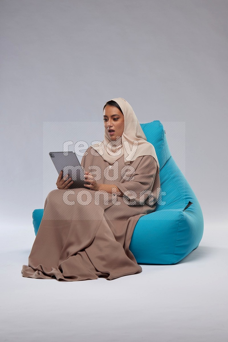 A Saudi woman sitting on a blue beanbag and working on tablet