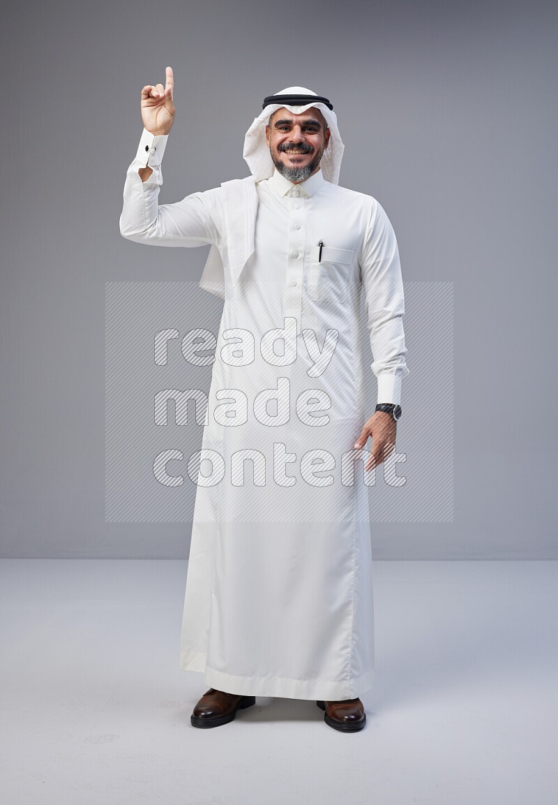 Saudi man Wearing Thob and white Shomag standing interacting with the camera on Gray background