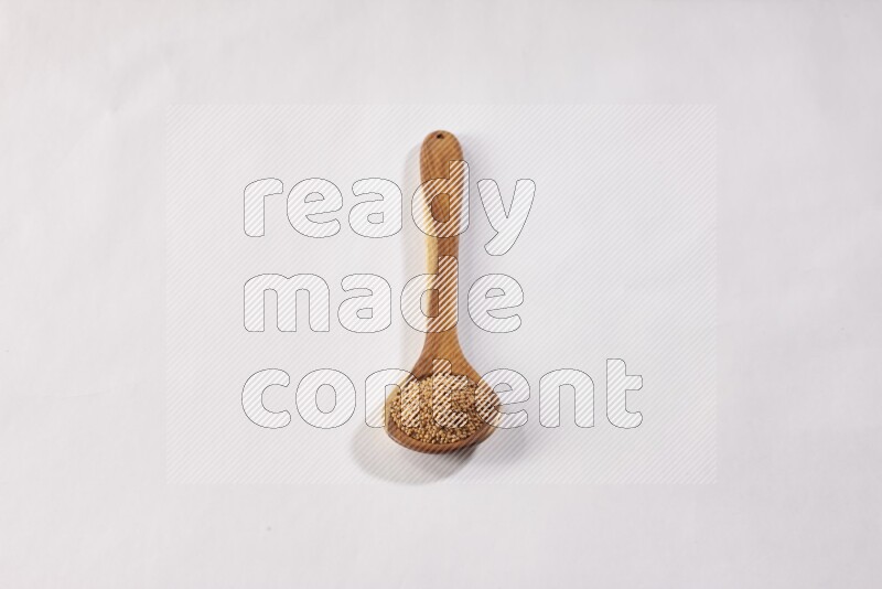 ملعقة خشبية كبيرة ممتلئة ببذور الخردل علي خلفية بيضاء