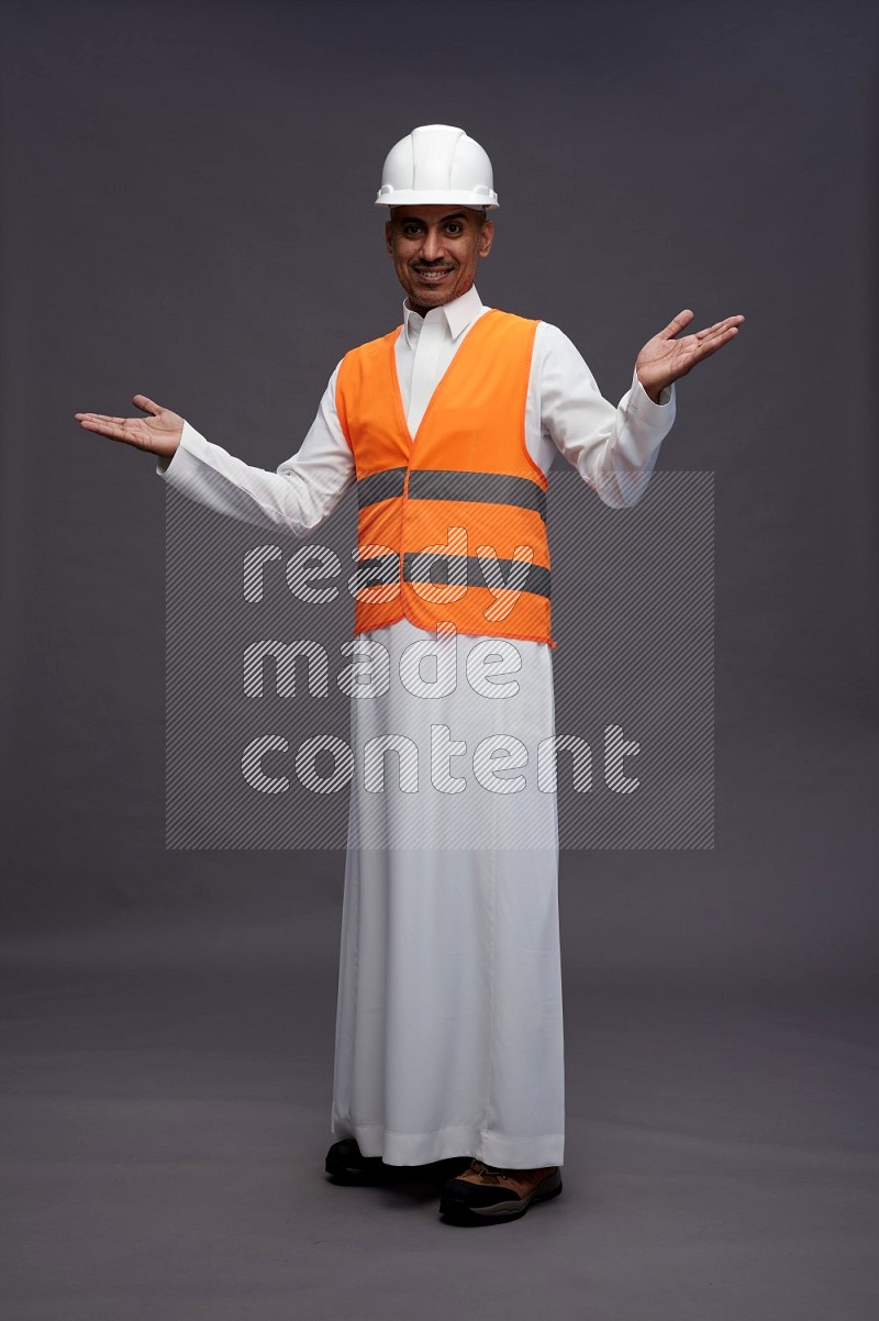 Saudi man wearing thob with engineer vest standing interacting with the camera on gray background