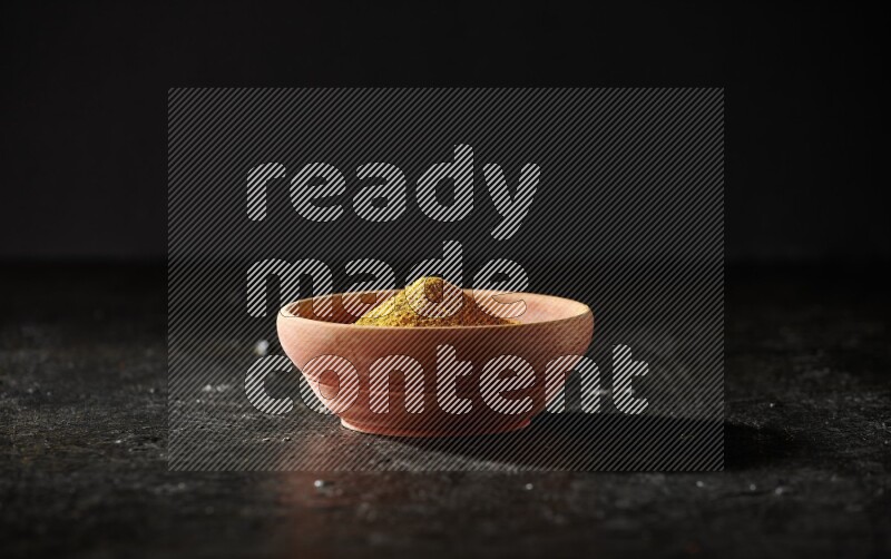 طبق خشبي ممتلئ ببودرة الكركم مع أصابع الكركم المجففة على خلفية سوداء