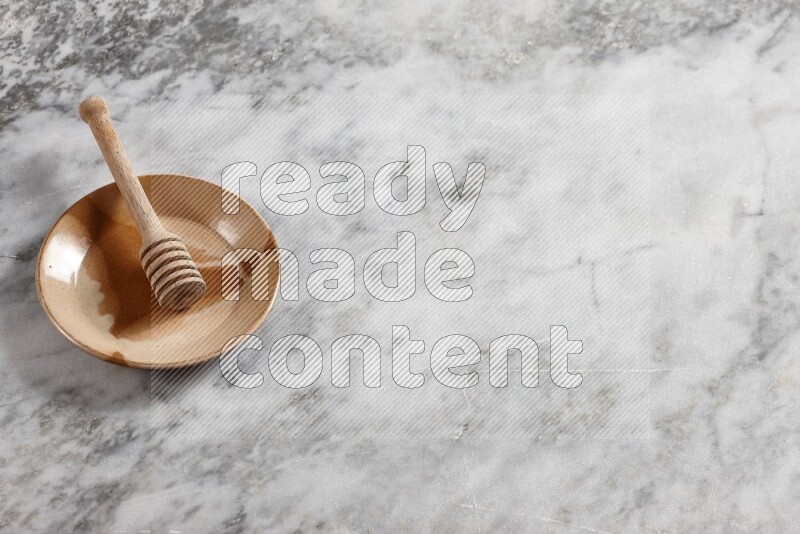 Multicolored pottery plate with wooden honey dipper in it on grey marble background