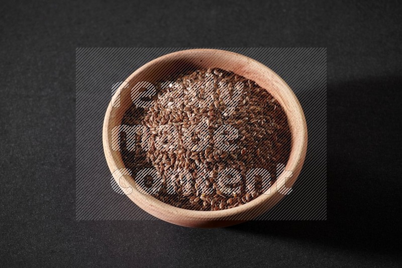 A wooden bowl full of flaxseeds on a black flooring