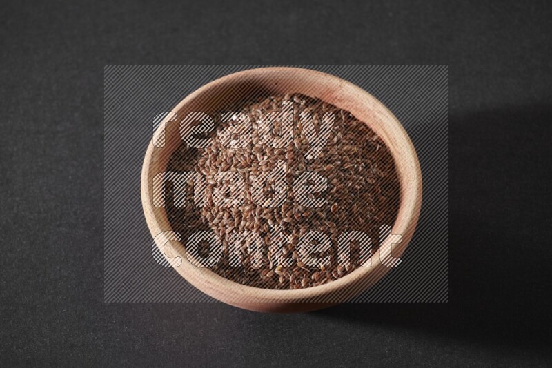 A wooden bowl full of flaxseeds on a black flooring