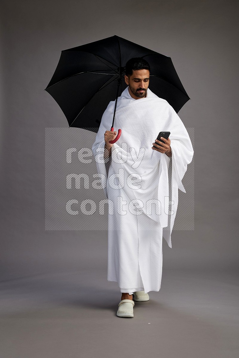 A man wearing Ehram Standing holding umbrella on gray background