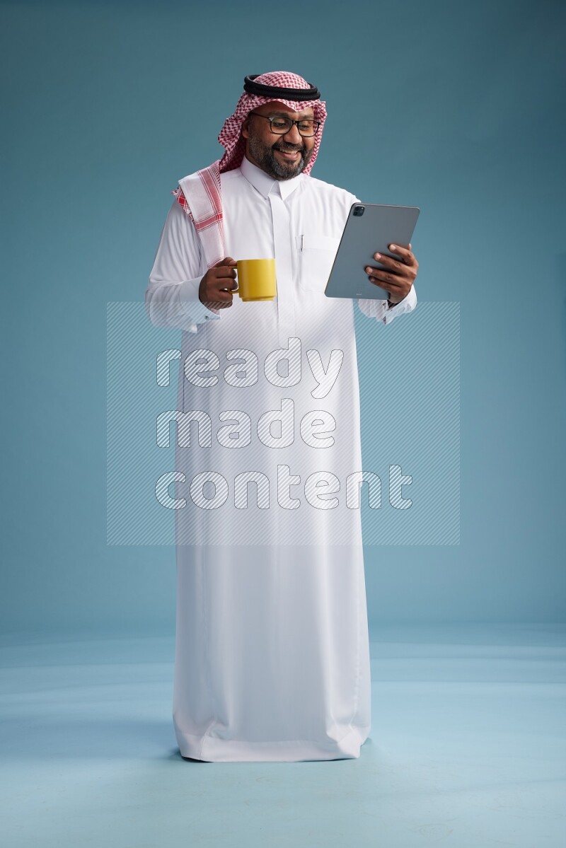 Saudi Man with shimag Standing holding a tablet on blue background