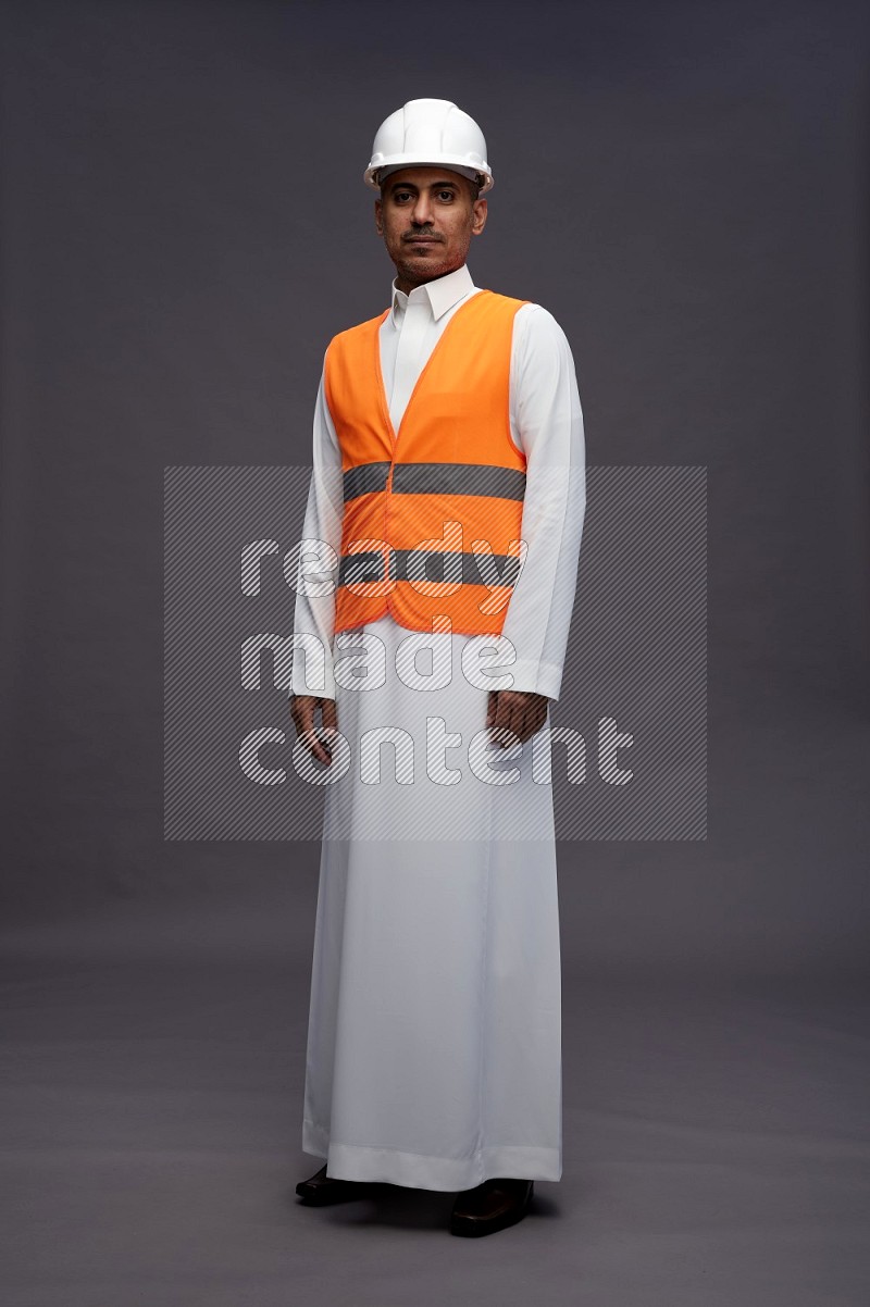 Saudi man wearing thob with engineer vest standing interacting with the camera on gray background