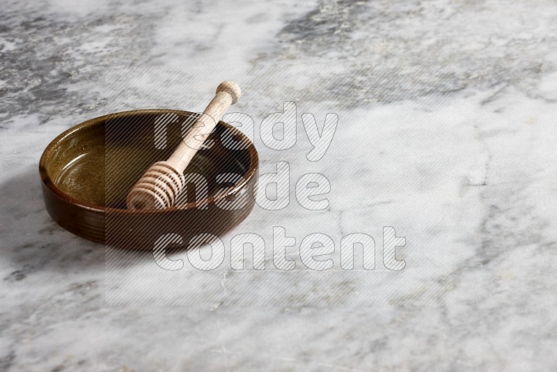 Multicolored Pottery Oven Plate with wooden honey handle in it, on grey marble flooring, 45 degree angel