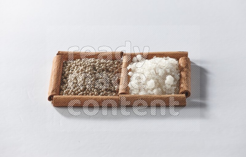 مربعان من أعواد القرفة ممتلئان بحبوب الفلفل الأبيض والملح الأبيض علي خلفية بيضاء