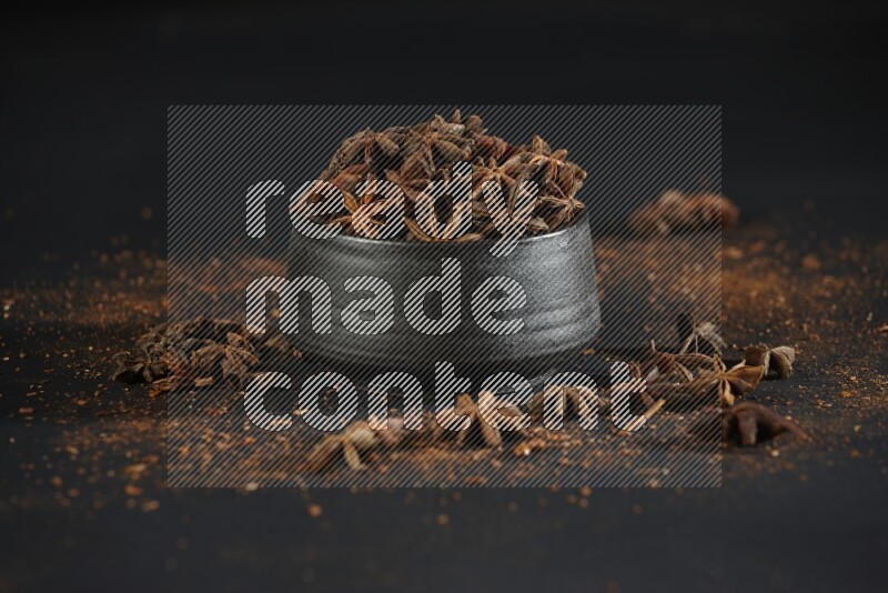 Star Anise in a black bowl with sprinkled anise on black flooring