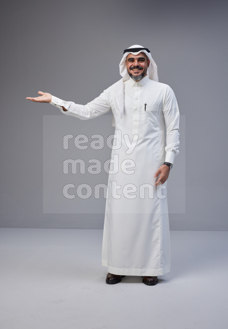 Saudi man Wearing Thob and white Shomag standing interacting with the camera on Gray background