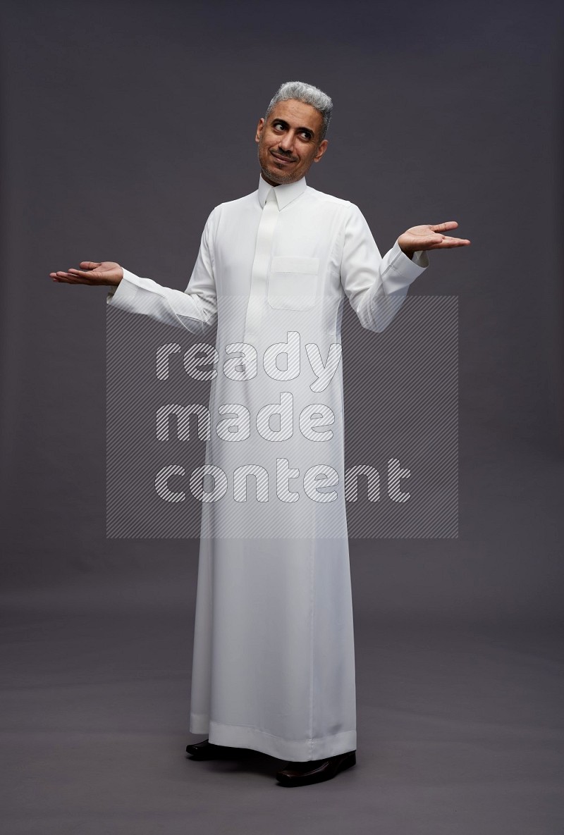 Saudi man wearing thob standing interacting with the camera on gray background