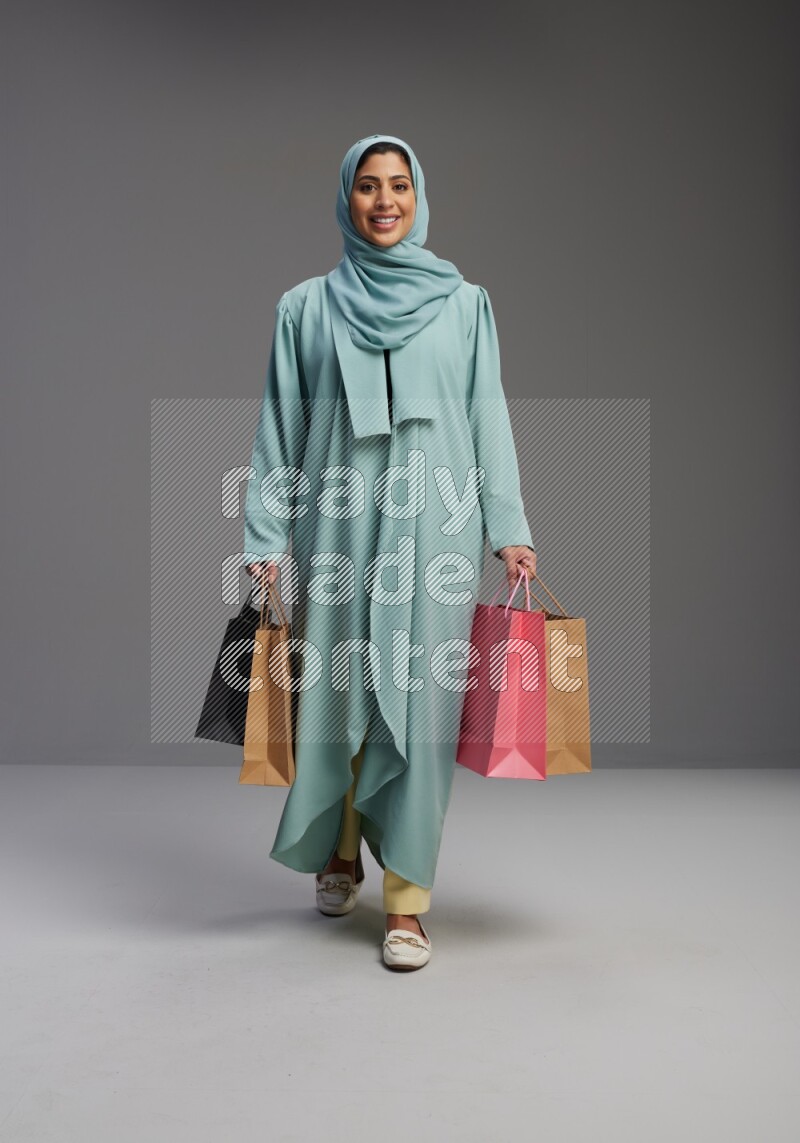 Saudi Woman wearing Abaya standing holding shopping bag on Gray background