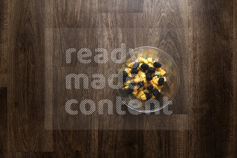 A glass bowl full of tuna, avocado, mango, blackberry and strawberry on wooden background