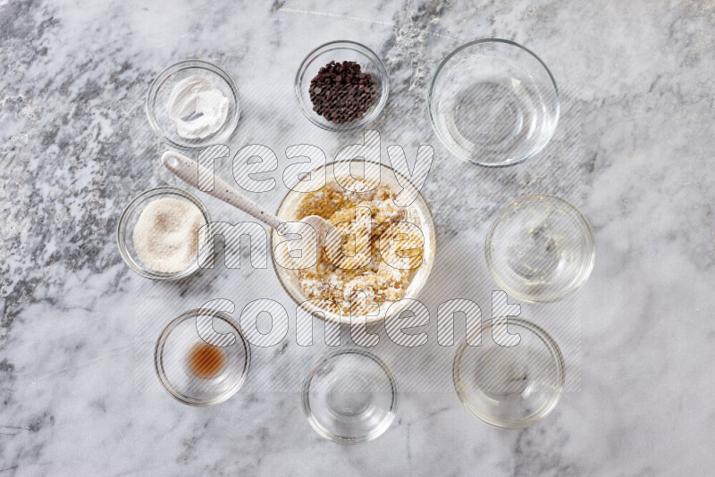 Cookies step by step with its ingredient, flour, butter, brown sugar, egg, vanilla extract, white sugar, chocolate chips and baking soda on grey marble background