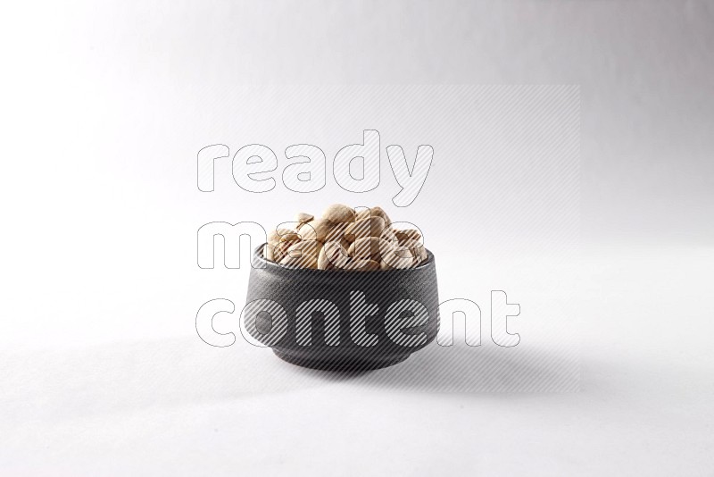 Pistachios in a black pottery bowl on white background