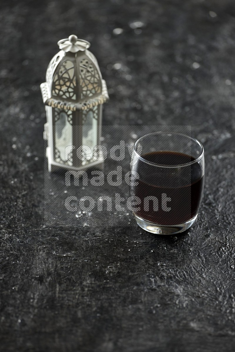 A white lantern with drinks, dates, nuts, prayer beads and quran on textured black background