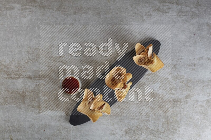 wonton cups with soy sauce ramkin on oval slate on grey textured counter top