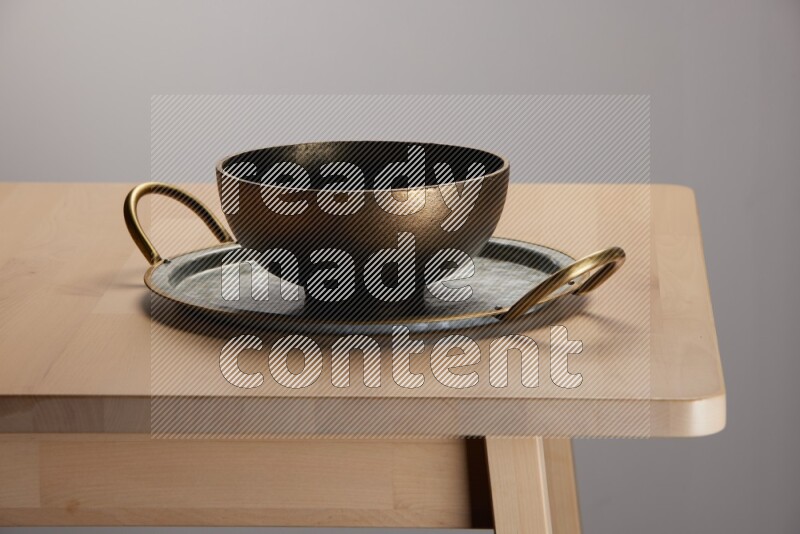 brass bowl placed on a rounded stainless steel metal tray with golden handels on the edge of wooden table