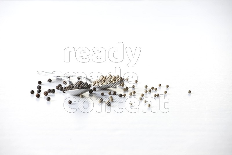 2 metal spoons full of black and white pepper beads with spreaded beads on white flooring