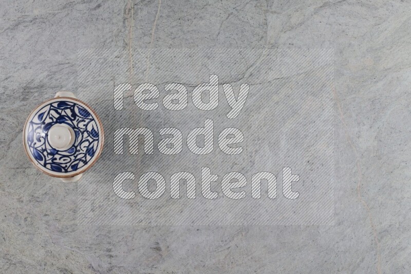 إناء فخاري متعدد الألوان مع غطائه على خلفية من الرخام الرمادي