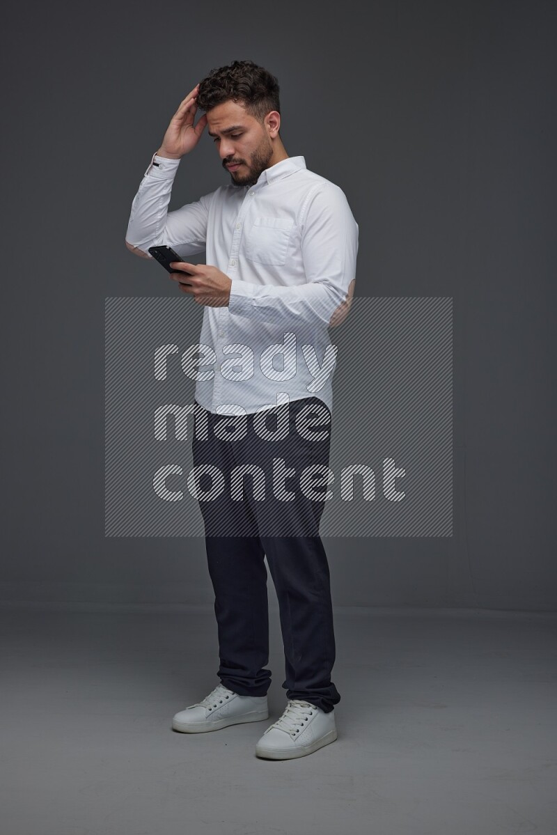 A man wearing smart casual standing and using his phone eye level on a gray background