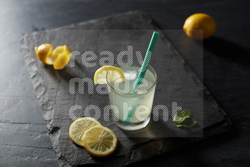 A glass of lemon juice with a straw on black background