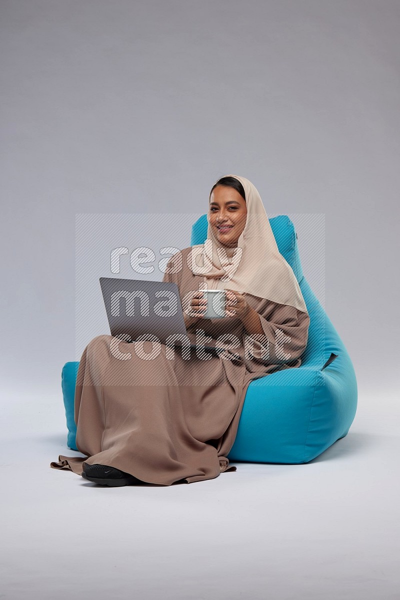 A Saudi woman sitting on a blue beanbag and working on laptop