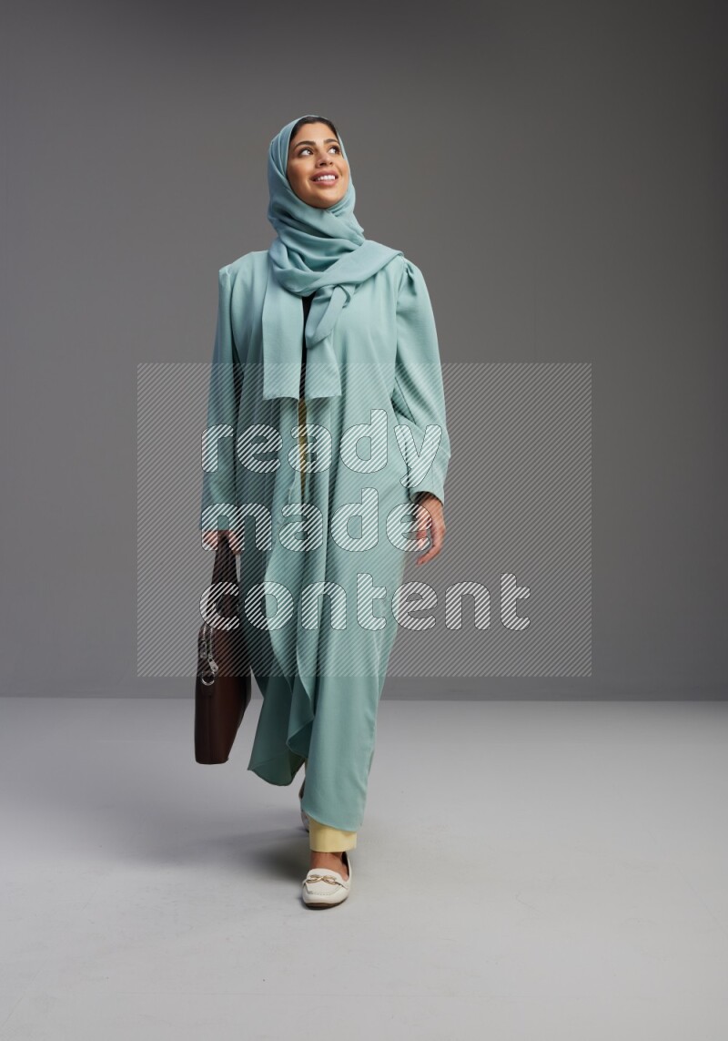 Saudi Woman wearing Abaya standing holding bag on Gray background