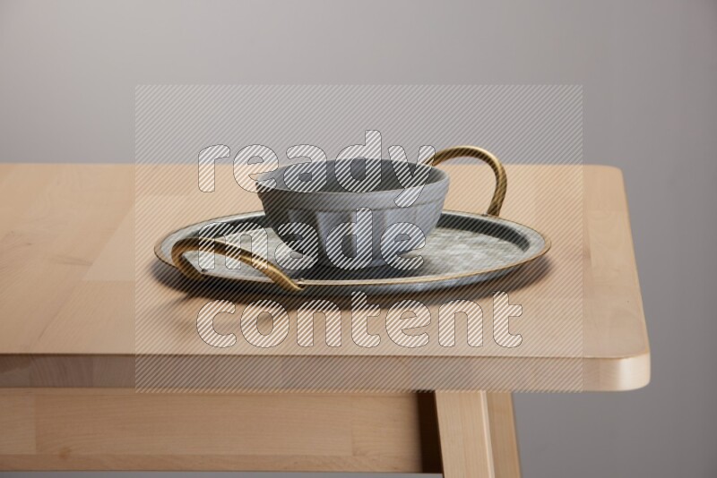 grey bowl placed on a rounded stainless steel tray with golden handels on the edge of wooden table