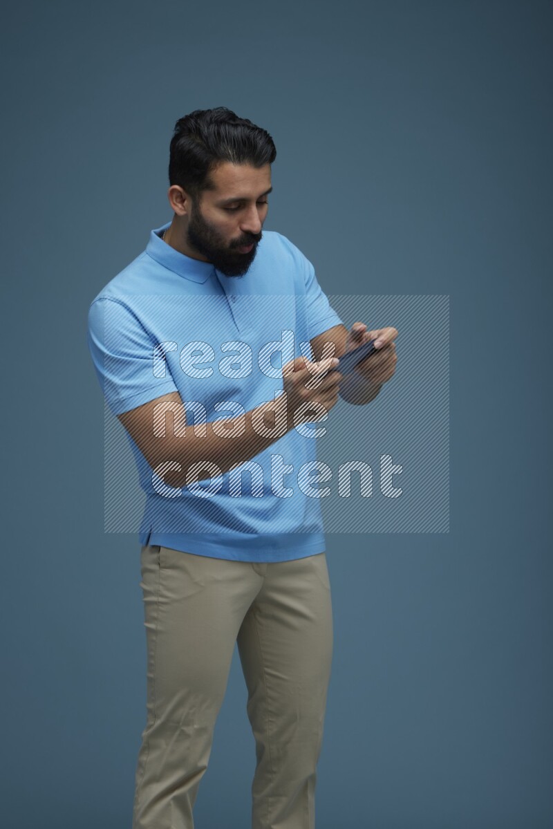 Man playing a game on his phone in a blue background wearing a Blue shirt