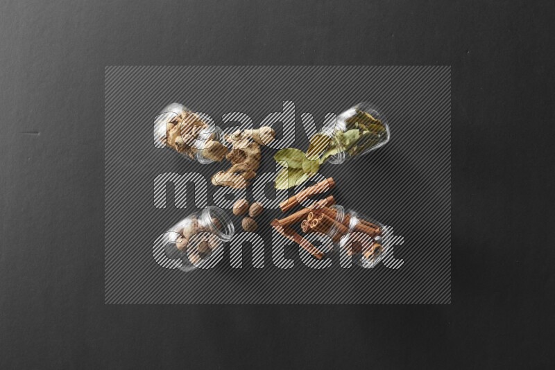 أوراق الغار وزنجبيل مجفف وقرفة وجوزة الطيب في أوعية زجاجية علي خلفية سوداء