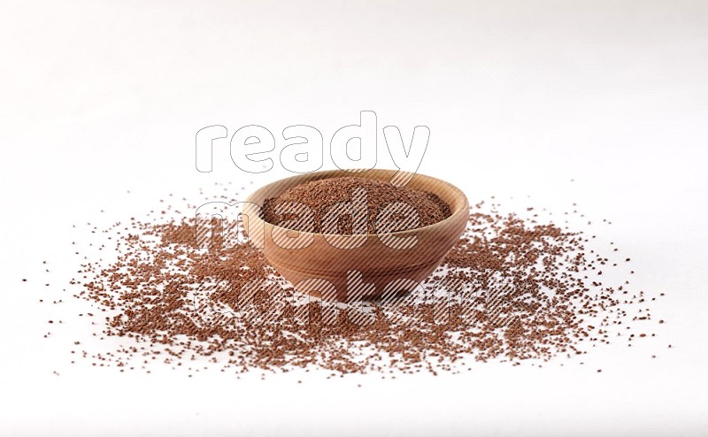 A wooden bowl full of garden cress seeds with more seeds spread on a white flooring