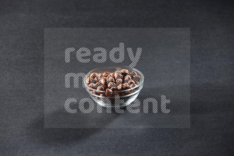 A glass bowl full of peeled hazelnuts on a black background in different angles