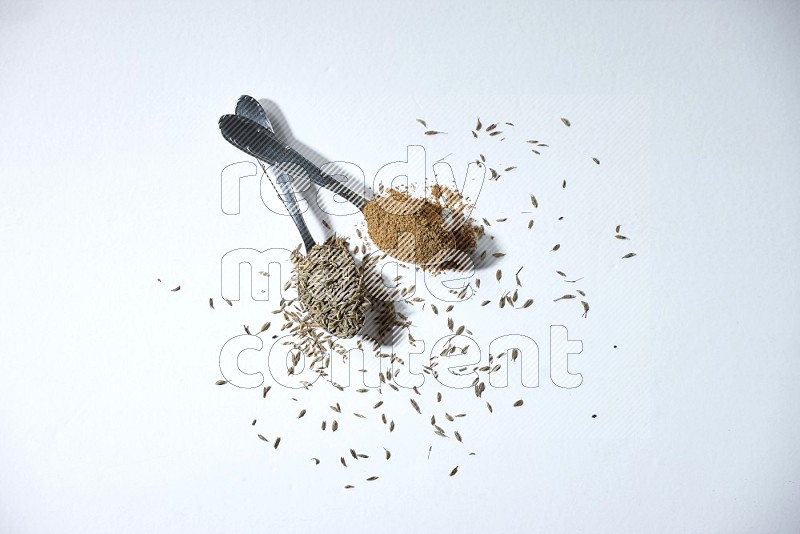 2 metal spoons full of cumin seeds and powder on white flooring