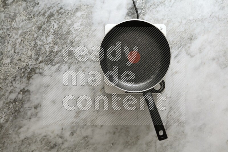 Frying pan on single electric stove on grey marble background
